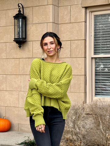 Lauren is standing in front of her home with a lovely green sweater on in the fall.