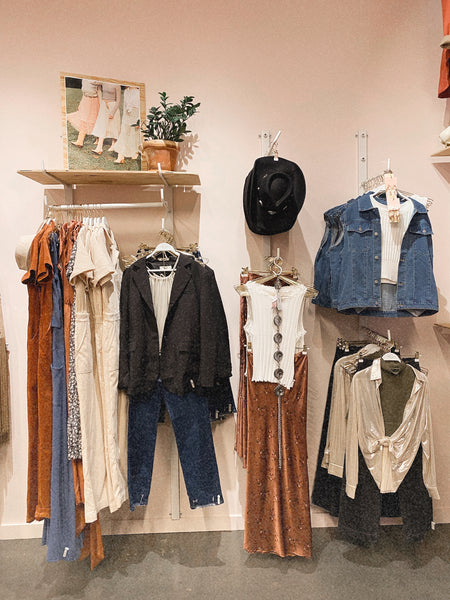 an image of a wall of clothing at molly green with a pink wall and concrete floors and a cute house plant on a shelf.