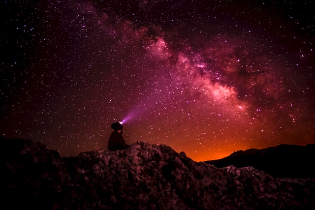 Mann leuchtet mit Taschenlampe in den roten Sternenhimmel