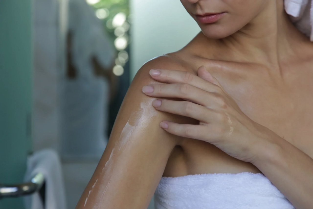 Woman applying lotion to her arm after a shower in a bathroom setting