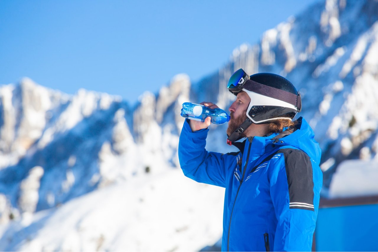 Male skier in blue jacket drinking water from bottle on snowy mountain landscape
