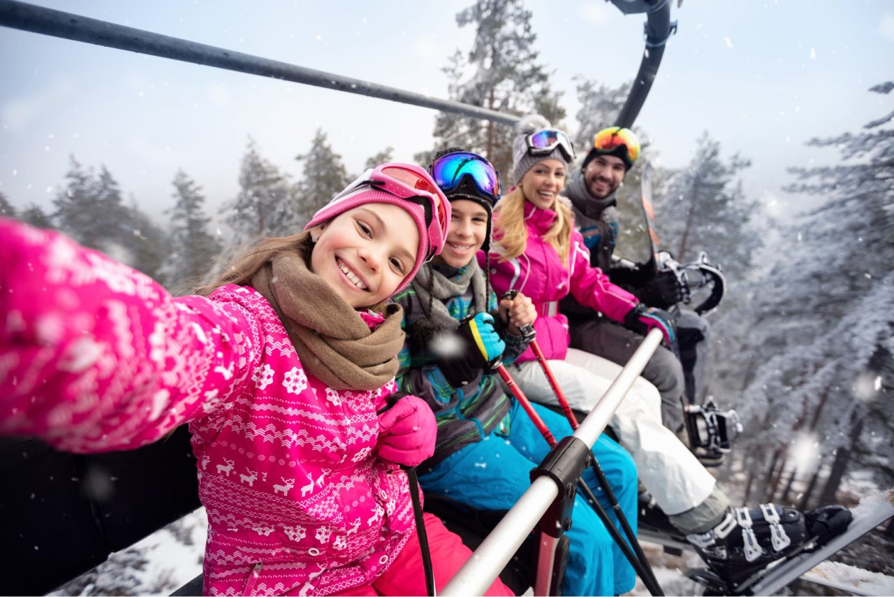 Family in ski gear taking a selfie on chairlift with snowy forest in background