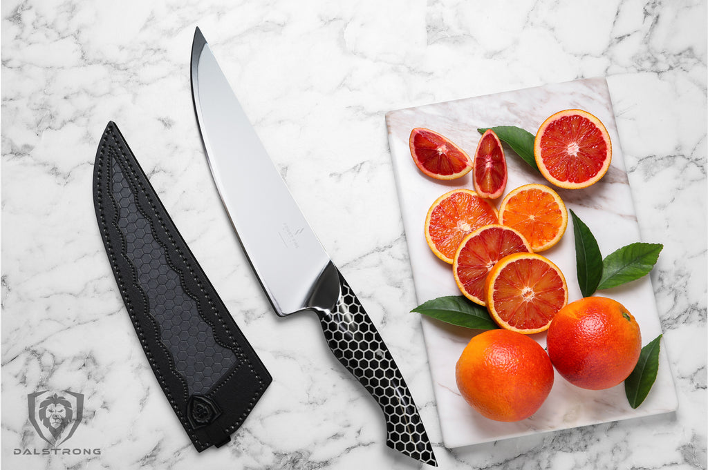 Sliced oranges next to a kitchen knife with a black scaled handle on a white counter 
