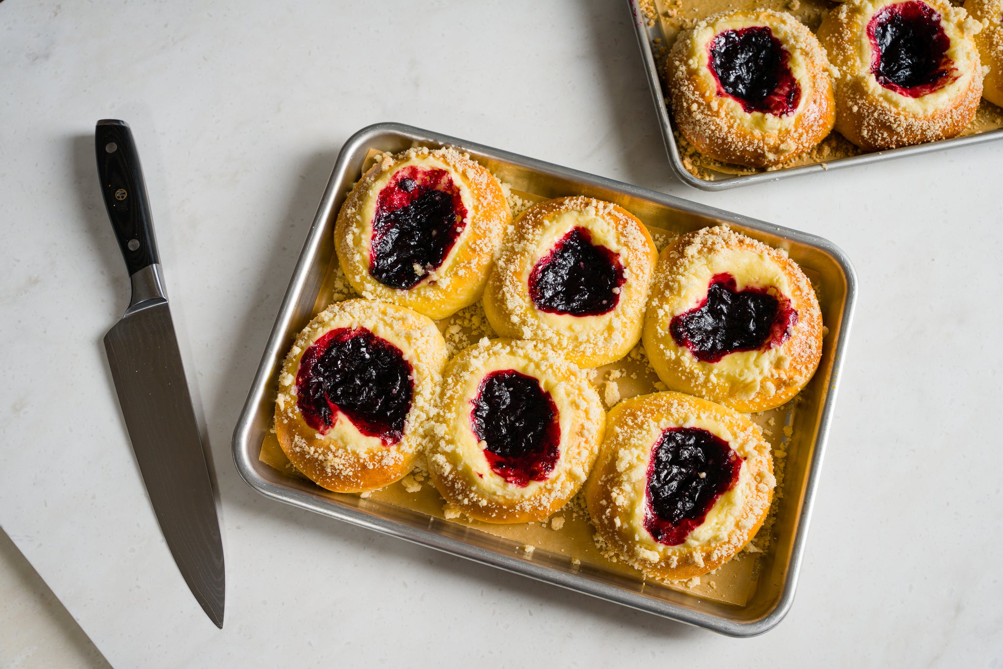 A tray of 6 cherry cheese kolaches fresh from the oven with a chef's knife to the left