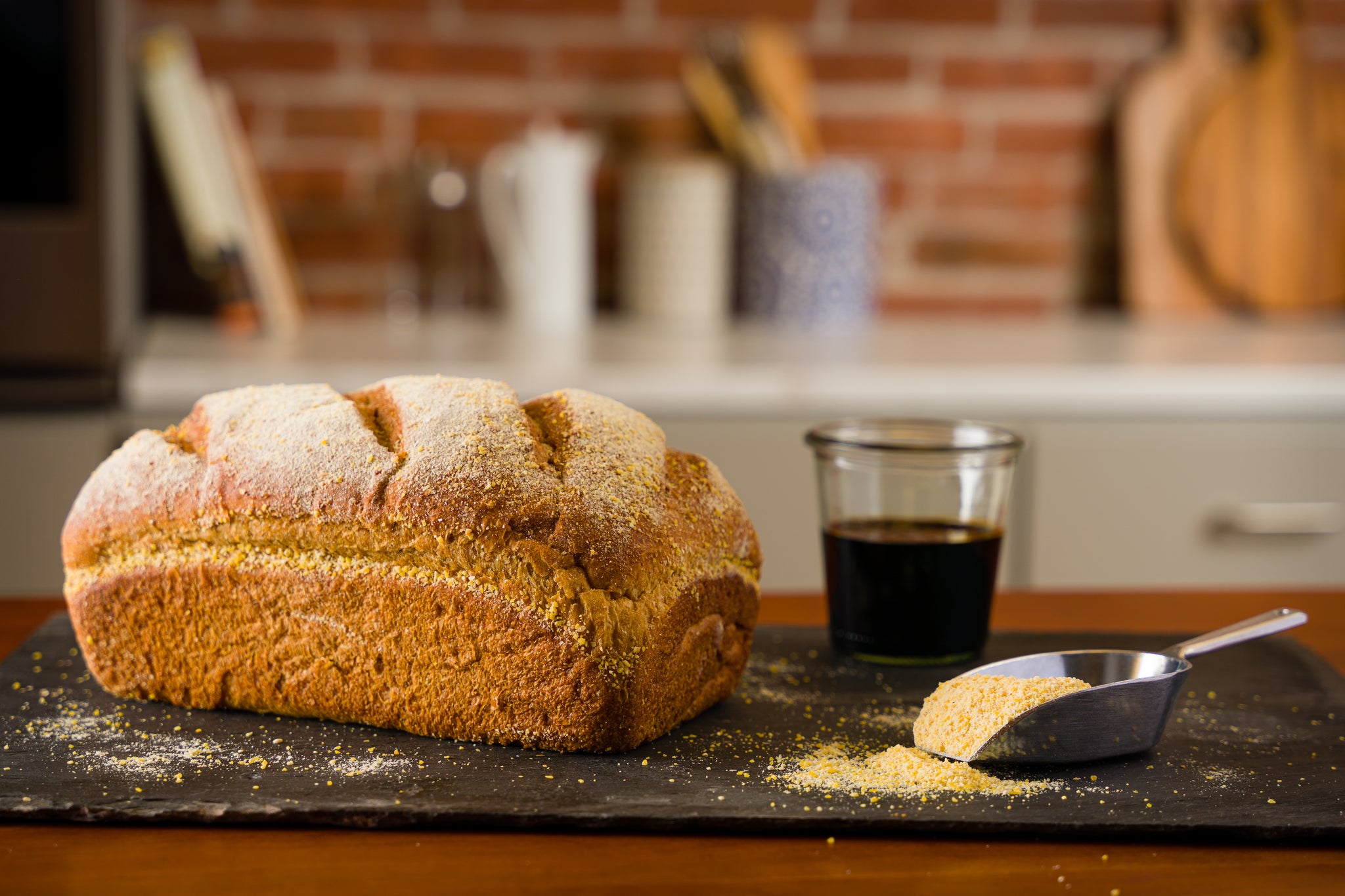 An anadama sandwich bread loaf sits on a kitchen counter with a jar of molasses and scoop of cornmeal to the right