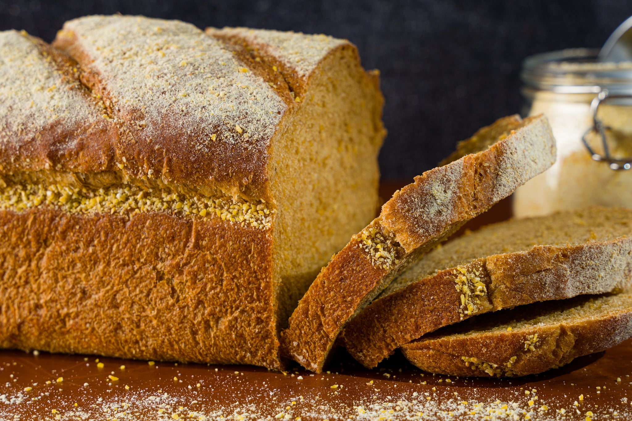 Slices of anadama bread falling from a loaf. A jar of cornmeal sits in the background.