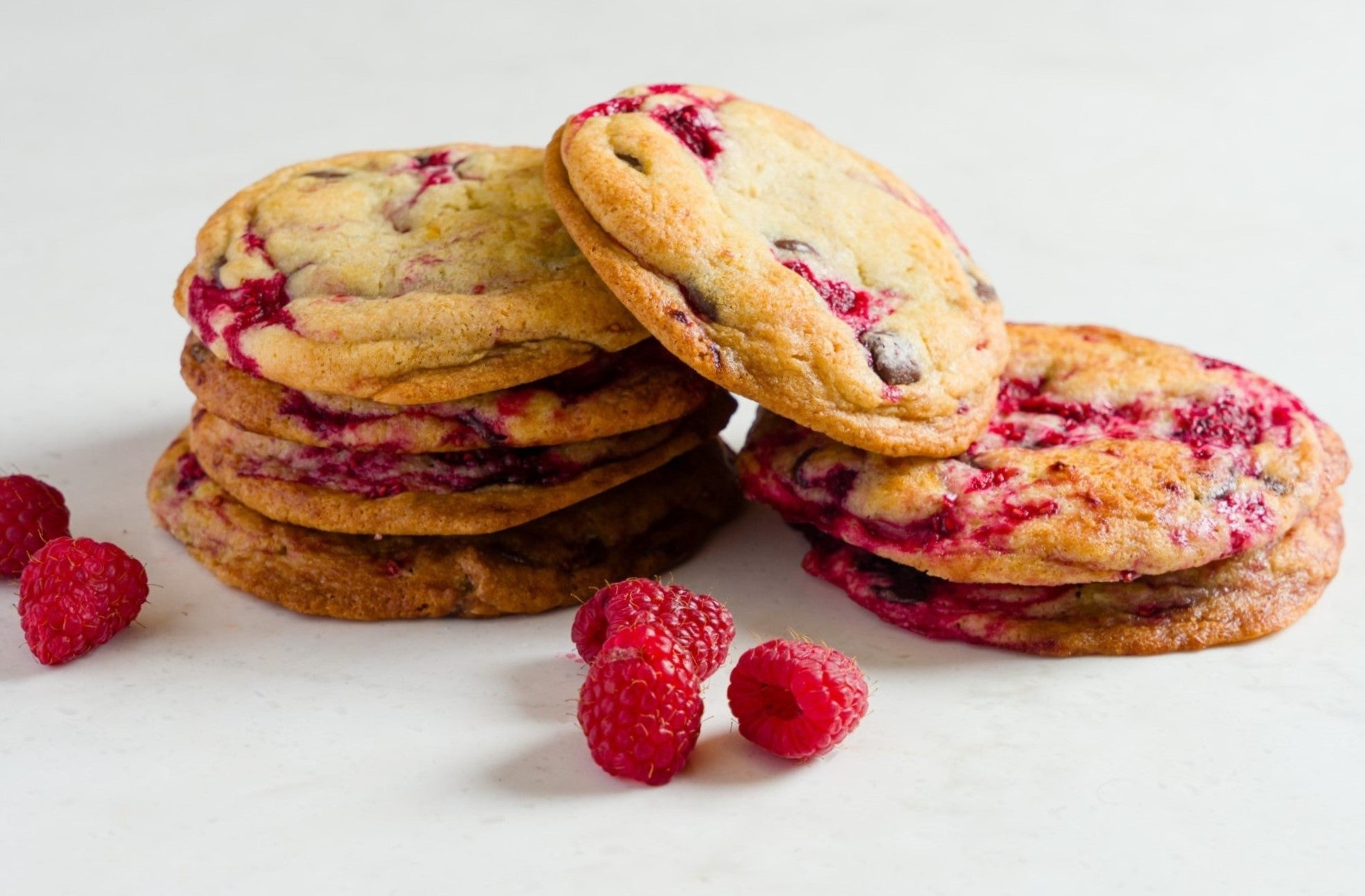 A stack of raspberry chocolate chip cookies on a white marble surface