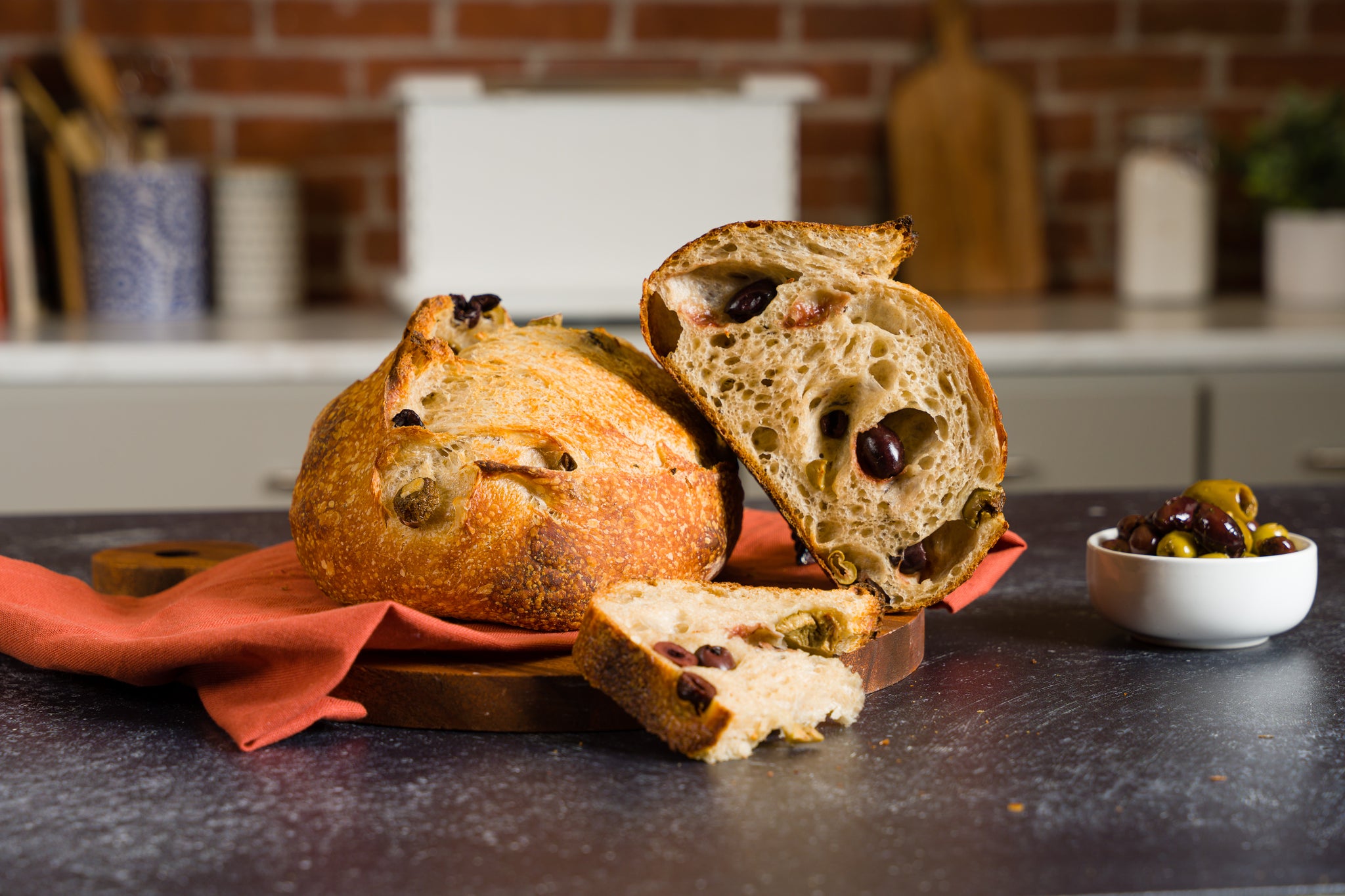 loaf of olive sourdough on kitchen counter with dish of mixed olives to the right