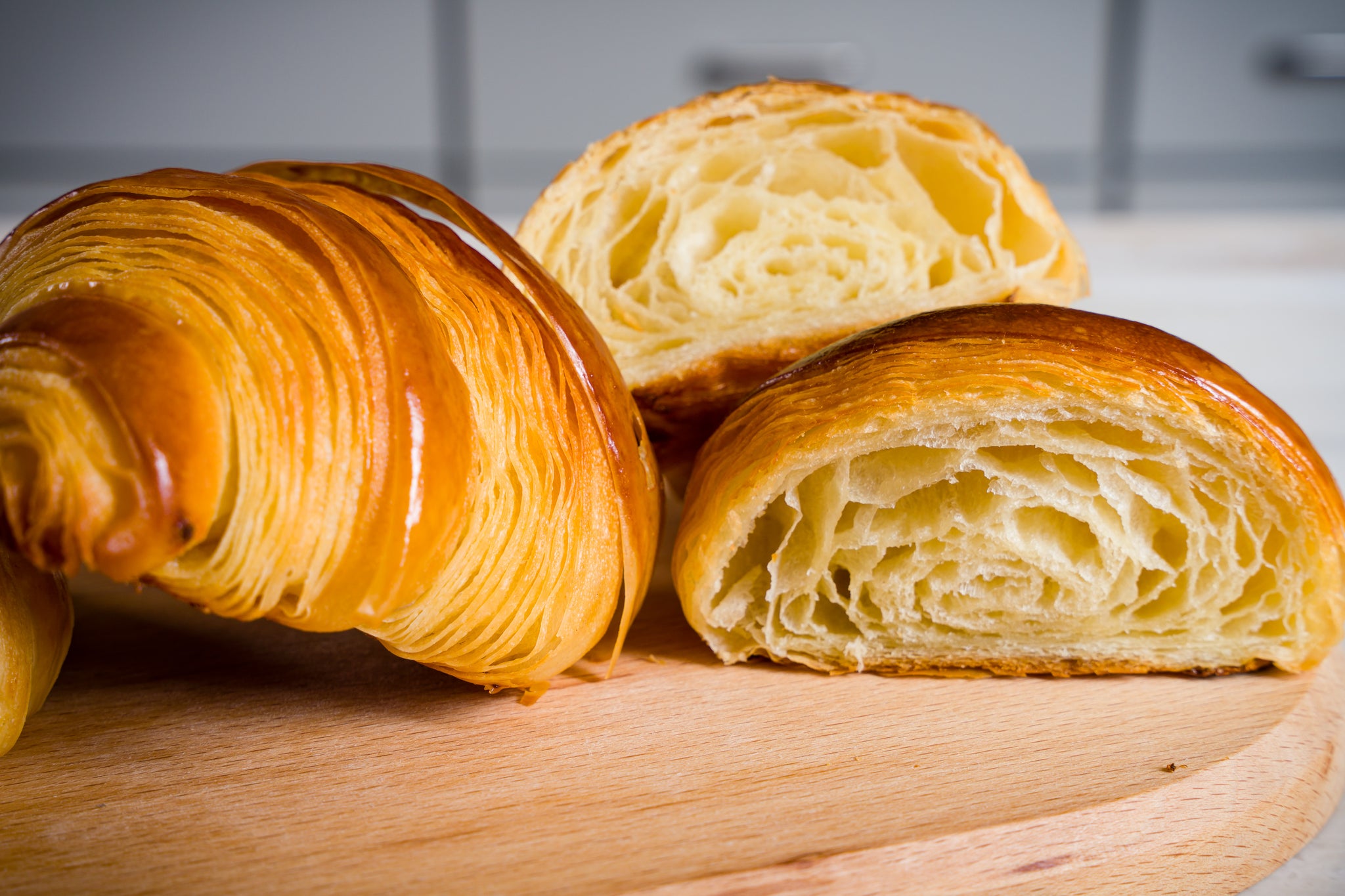 Two croissants sit on a wooden board. One is cut in half and the honeycomb interior is visible.