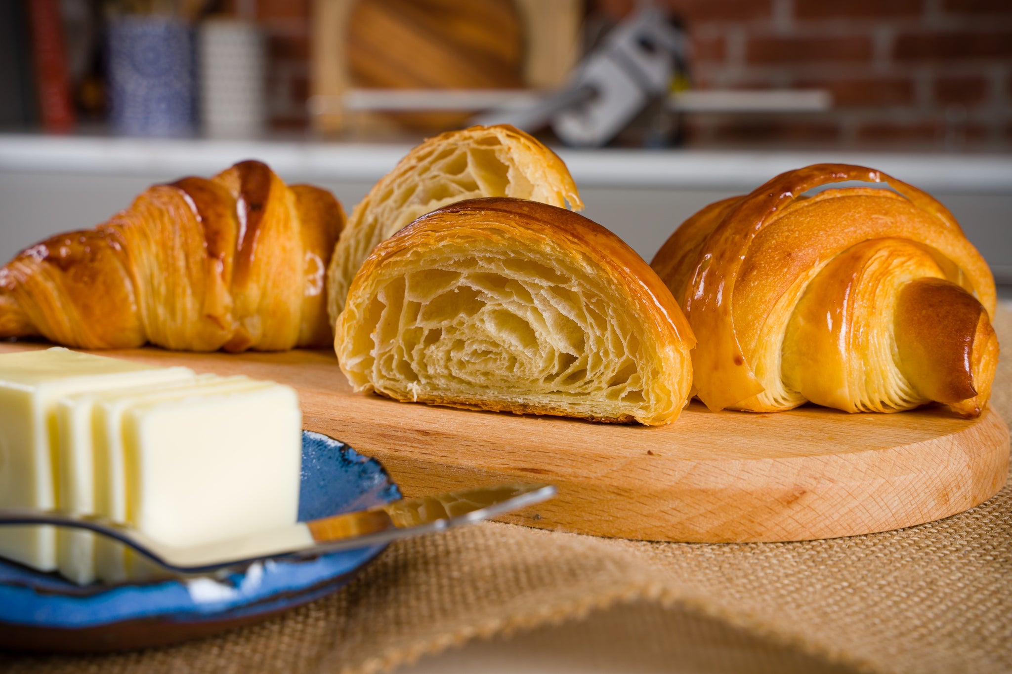 Flaky croissants on a kitchen counter with a dough sheeter in the background.