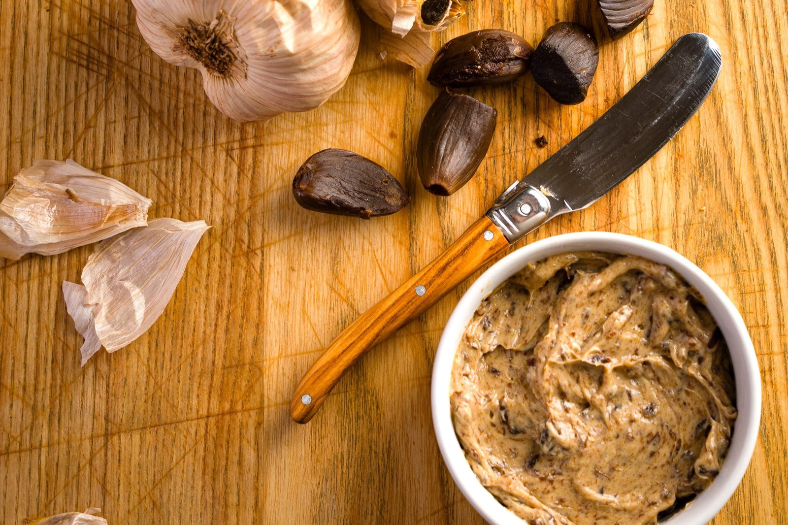 black garlic butter and black garlic cloves on a wooden counter top.