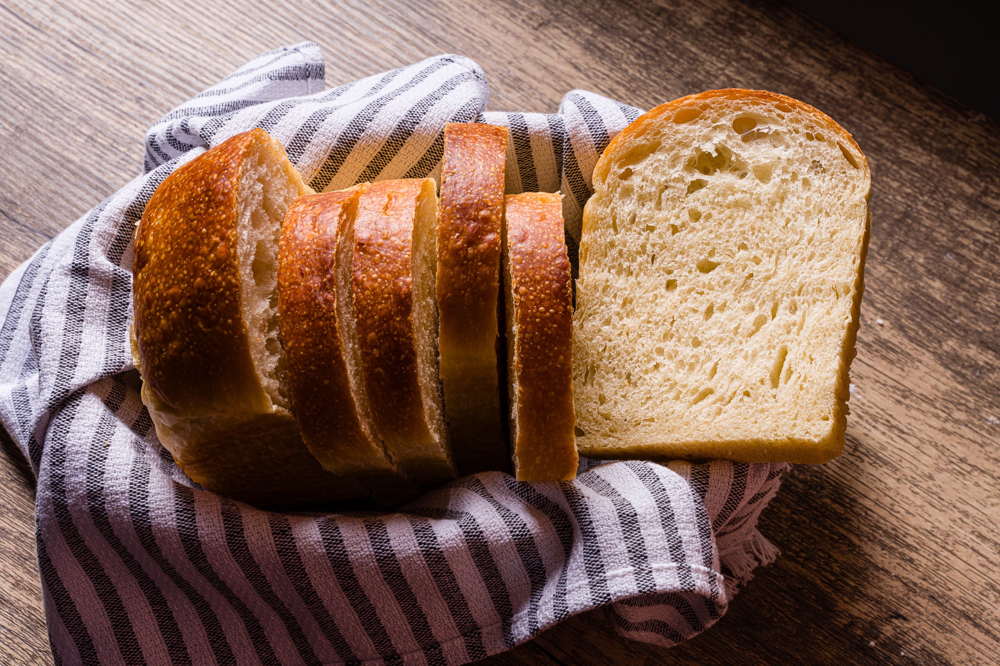 Sourdough sandwich bread slices in a basket lined with a striped cloth