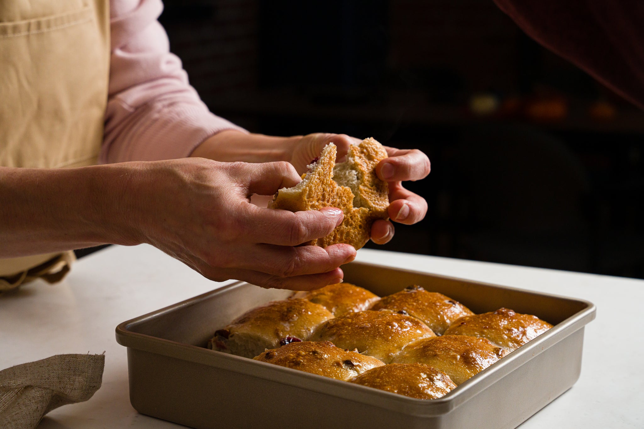 woman in an apron pulling a freshly baked dinner roll from a pan 