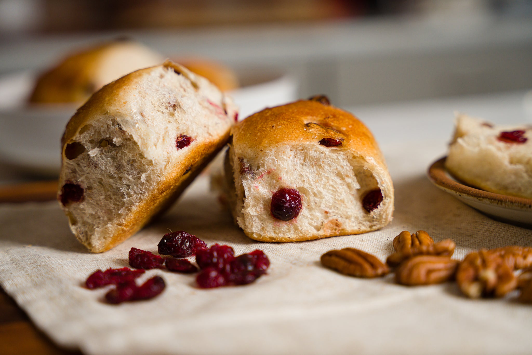 two cranberry pecans rolls on a beige linen napkin with pecans and dried cranberries scattered around