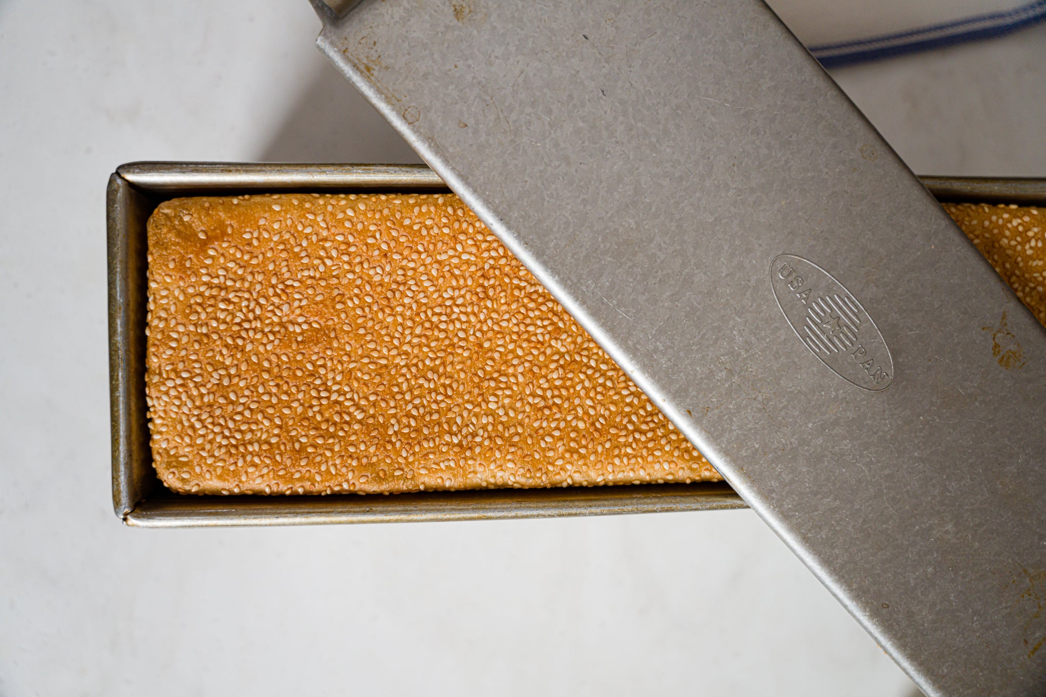 sesame coated loaf in a pullman pan with lid sitting askew