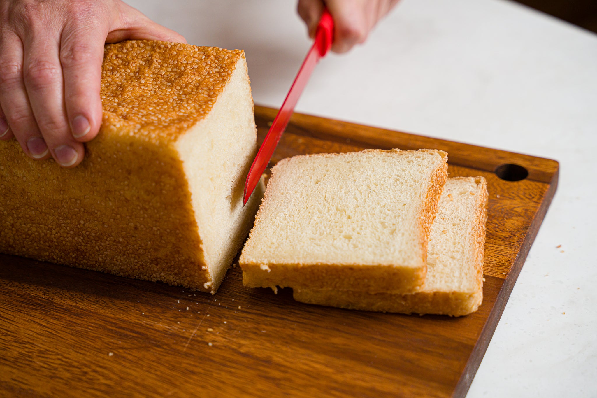 red serrated knife cutting slices off of a pain de mie