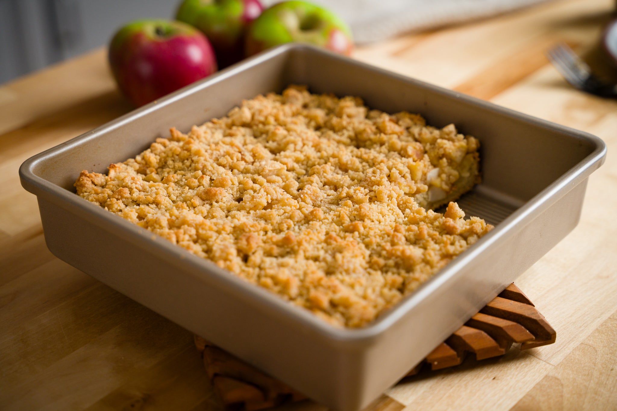 A square pan of apple streusel coffee cake sits on wooden counter