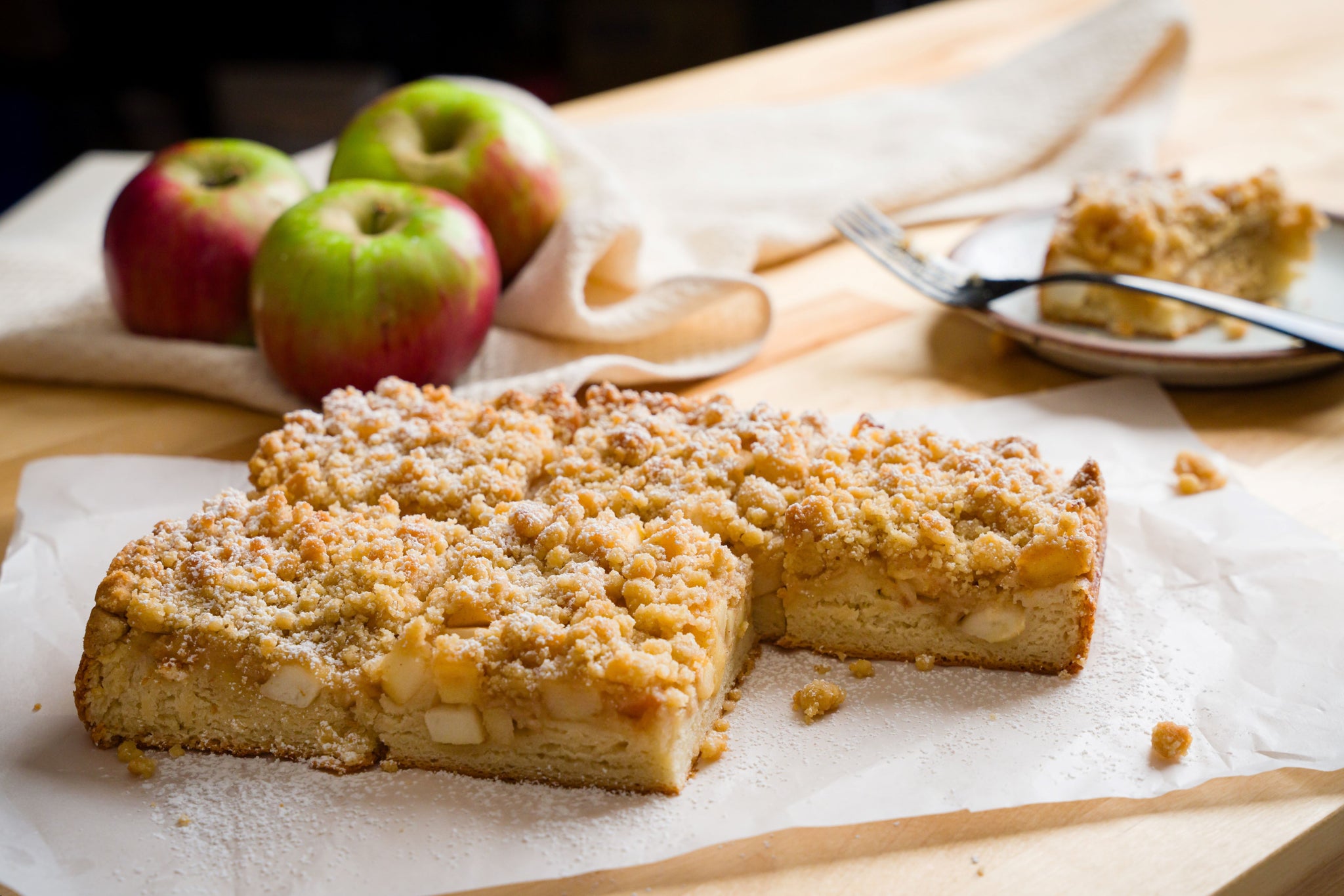 Pieces of German apple streusel cake on a wooden counter with apples in the background