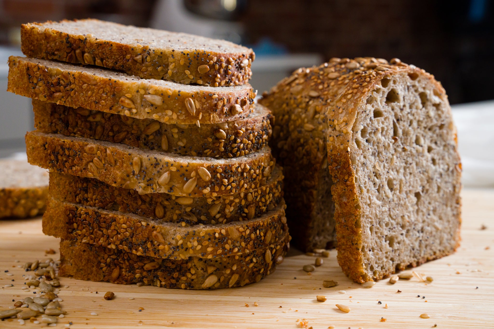 A tall stack of seeded sourdough bread slices on a wooden cutting board