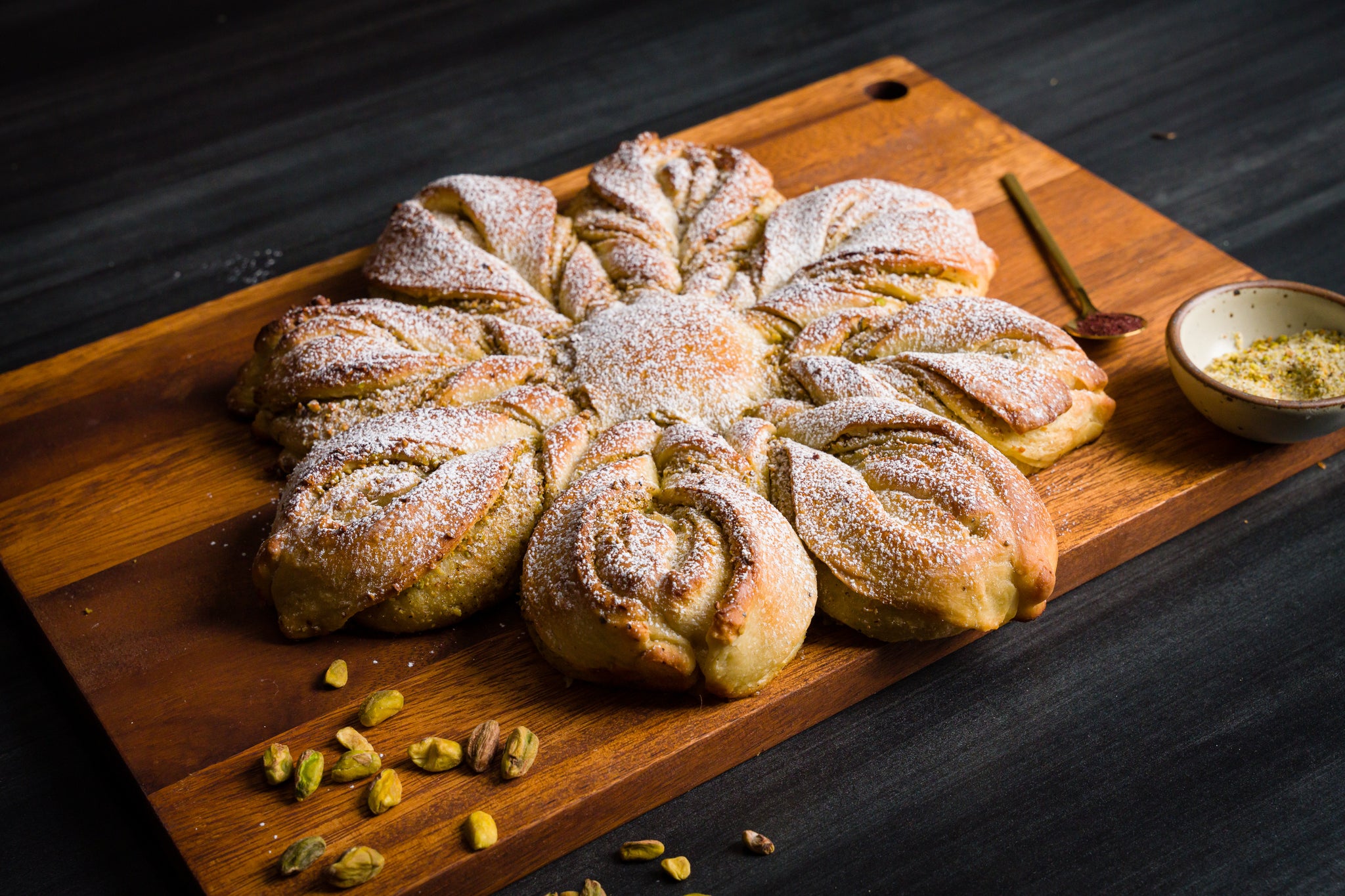 Pistachio Cardamom star shaped bread dusted with powdered sugar sitting on a wooden cutting board