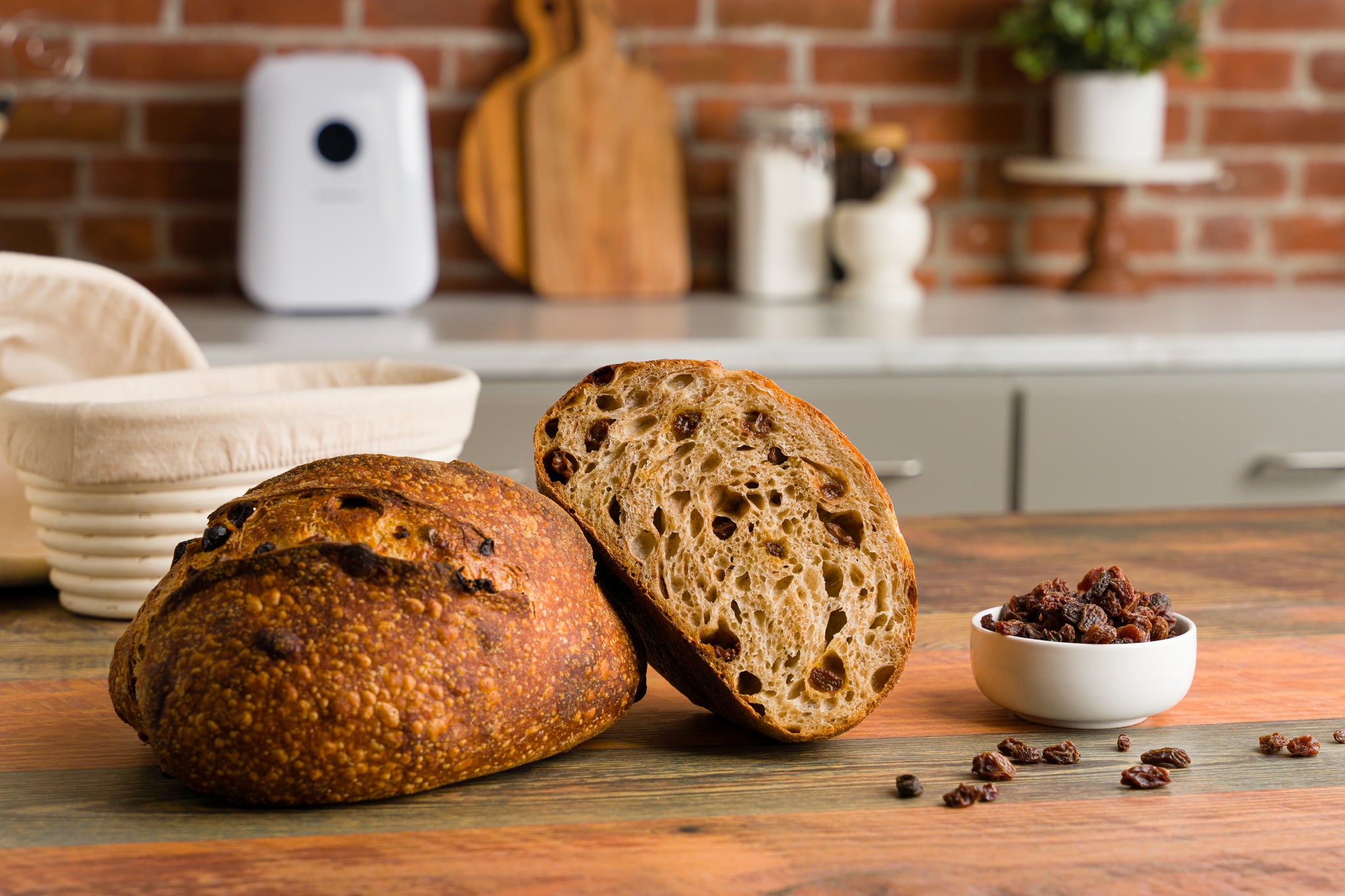 A half loaf of cinnamon raisin bread propped op on a whole loaf with a small bowl of raisins to the right side