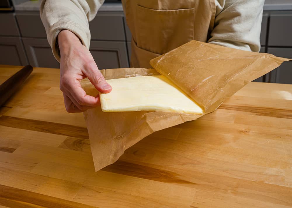 A hand holding a butter block on parchment paper.