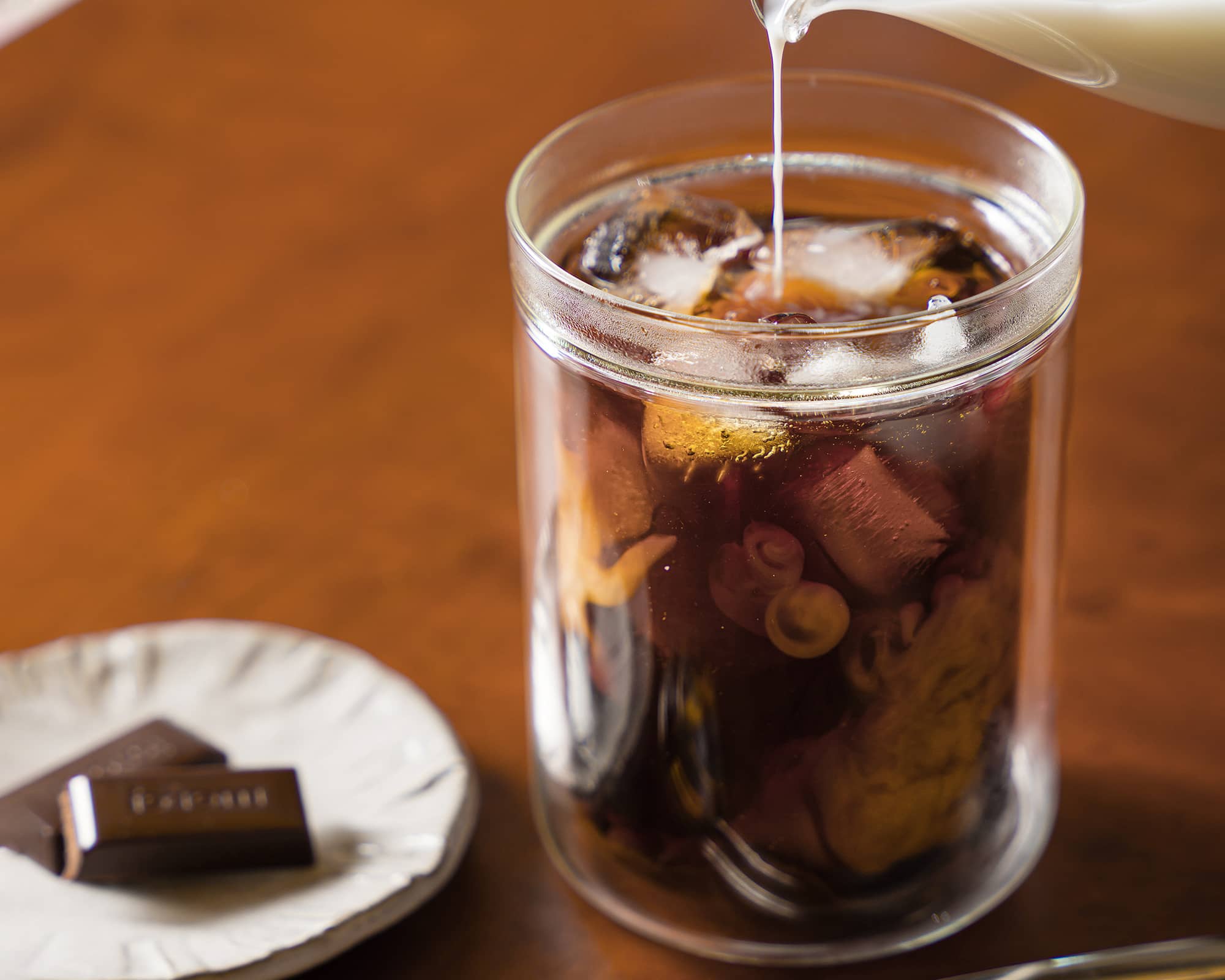 Iced coffee in the tumbler, milk is being poured.