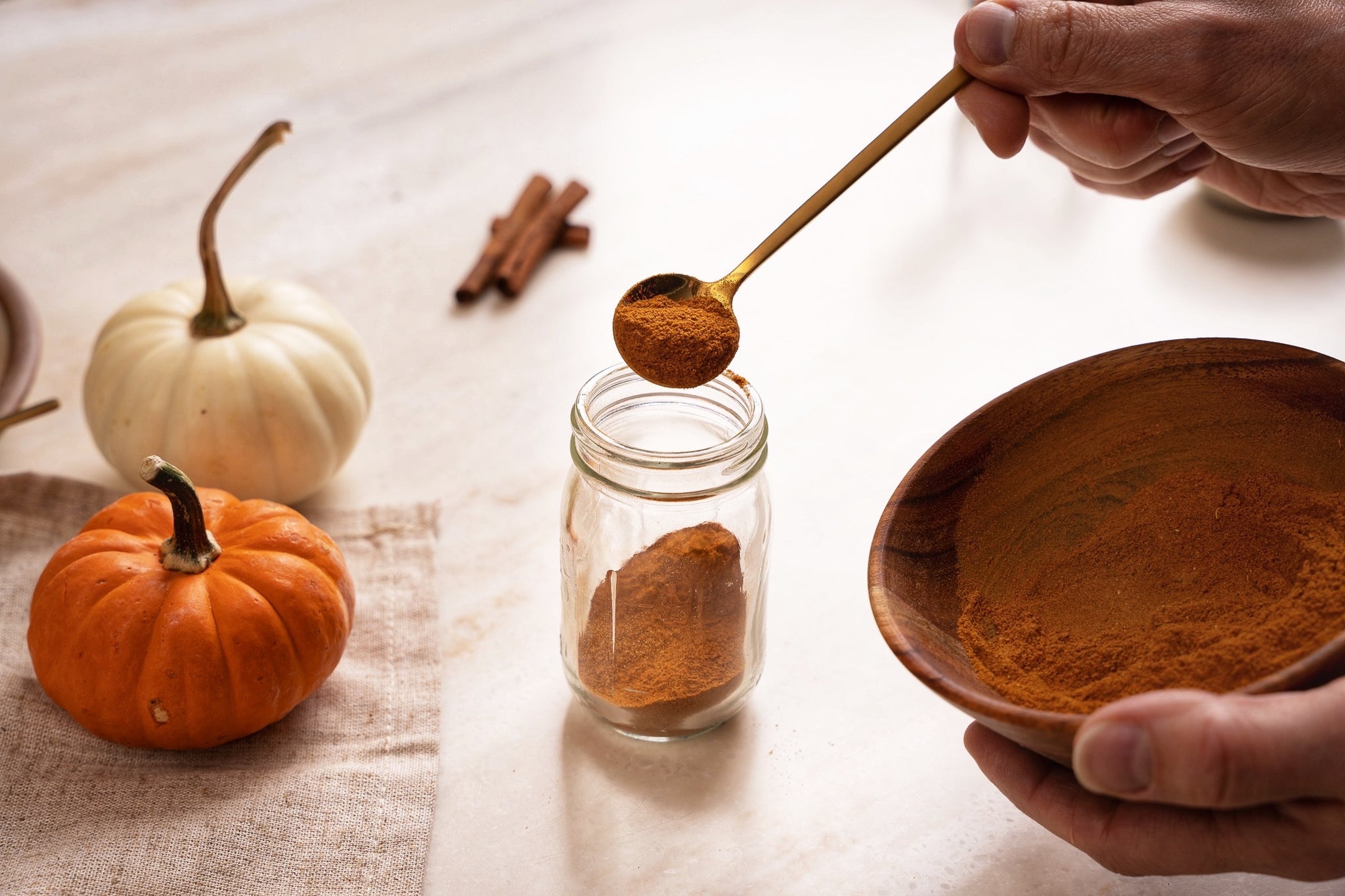 woman's hand using a small brass spoon to transfer pumpkin spice powder from wooden bowl to a spice jar
