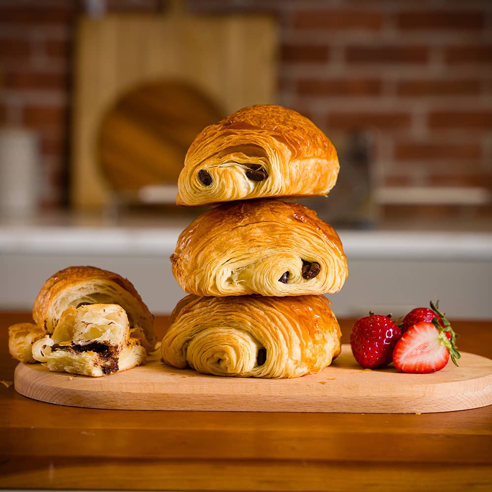 A stack of chocolate croissants on a wooden board