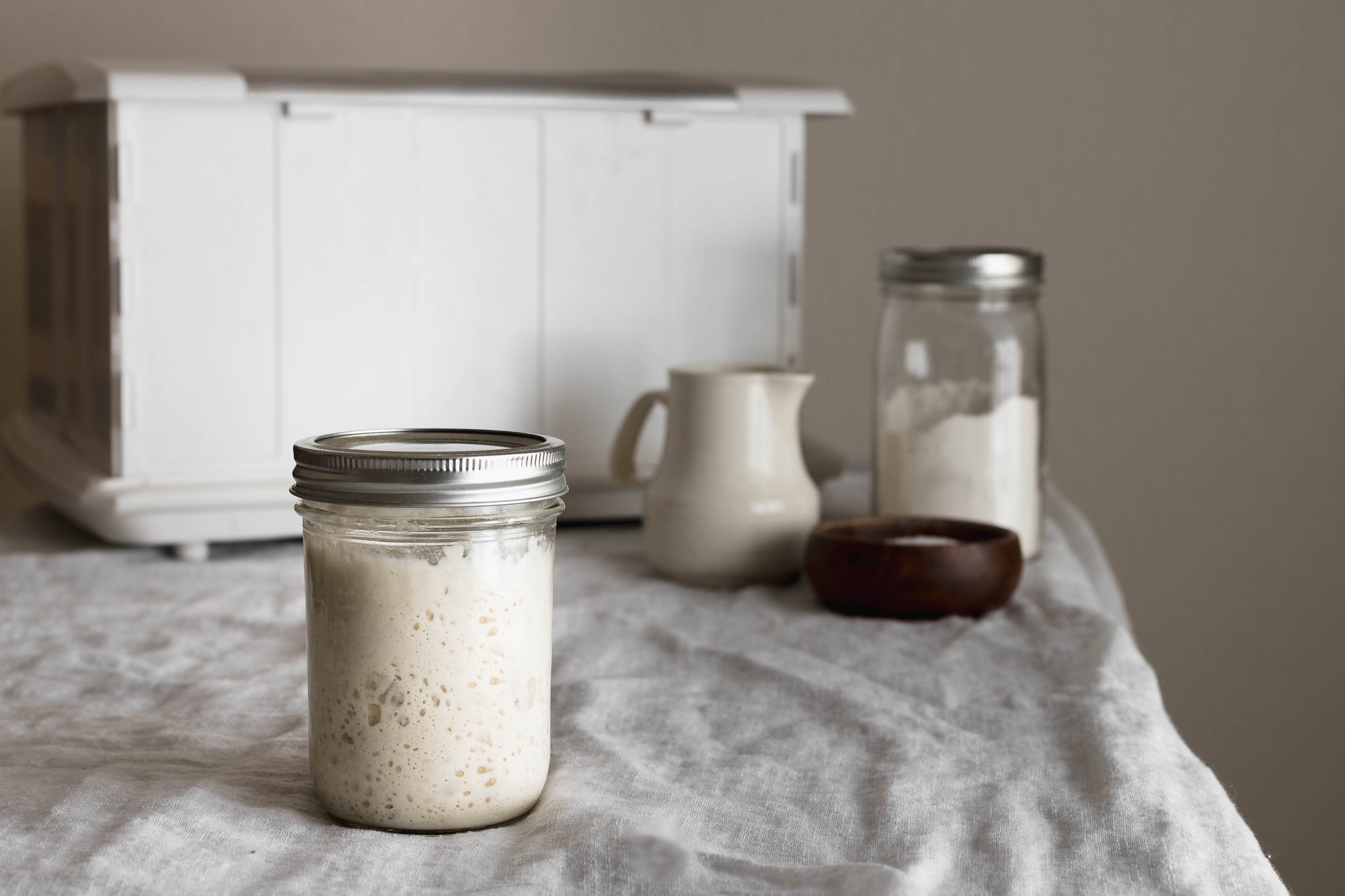 jar of sourdough starter on a table with proofer in the background