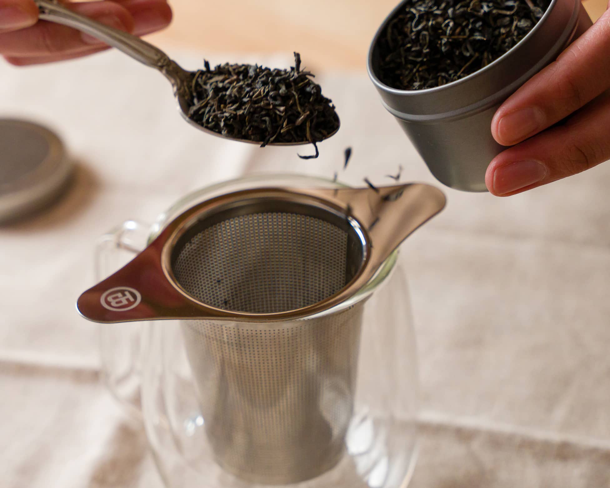 A spoonful of loose tea leaves being added to the tea infuser
