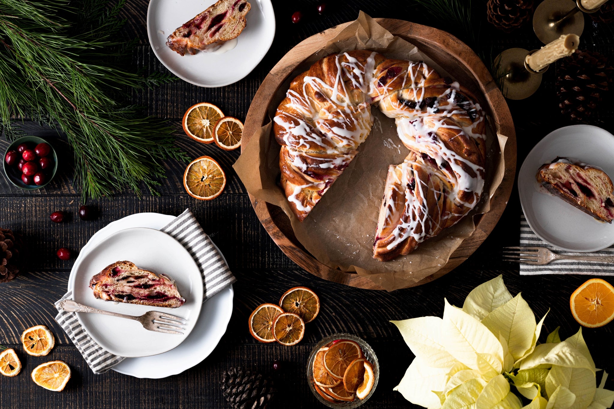 Overhead image of cranberry orange couronne on table with cut slices on plates and dried orange slices as decoration