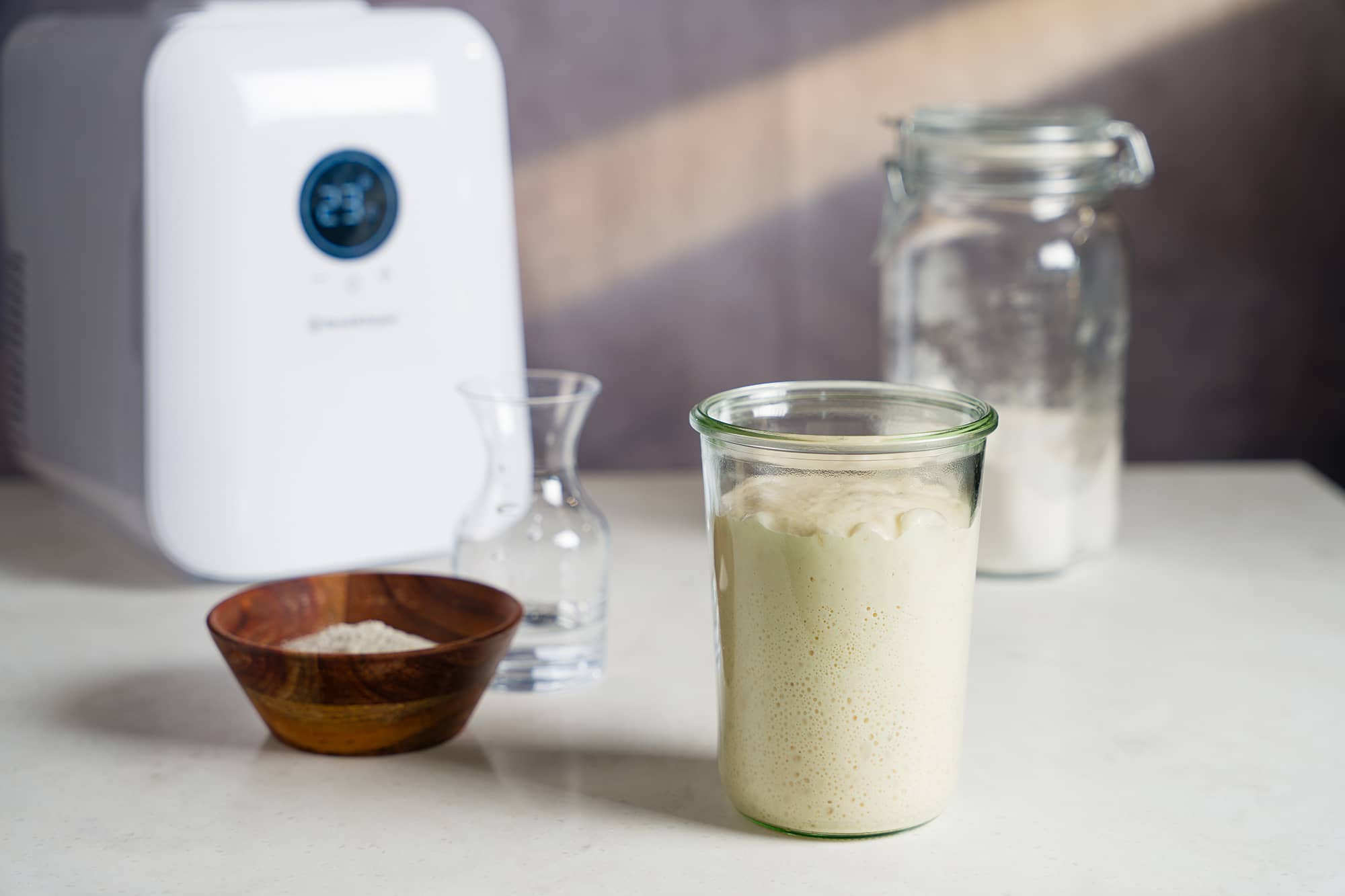 A jar of sourdough starter with Sourdough Home in the background