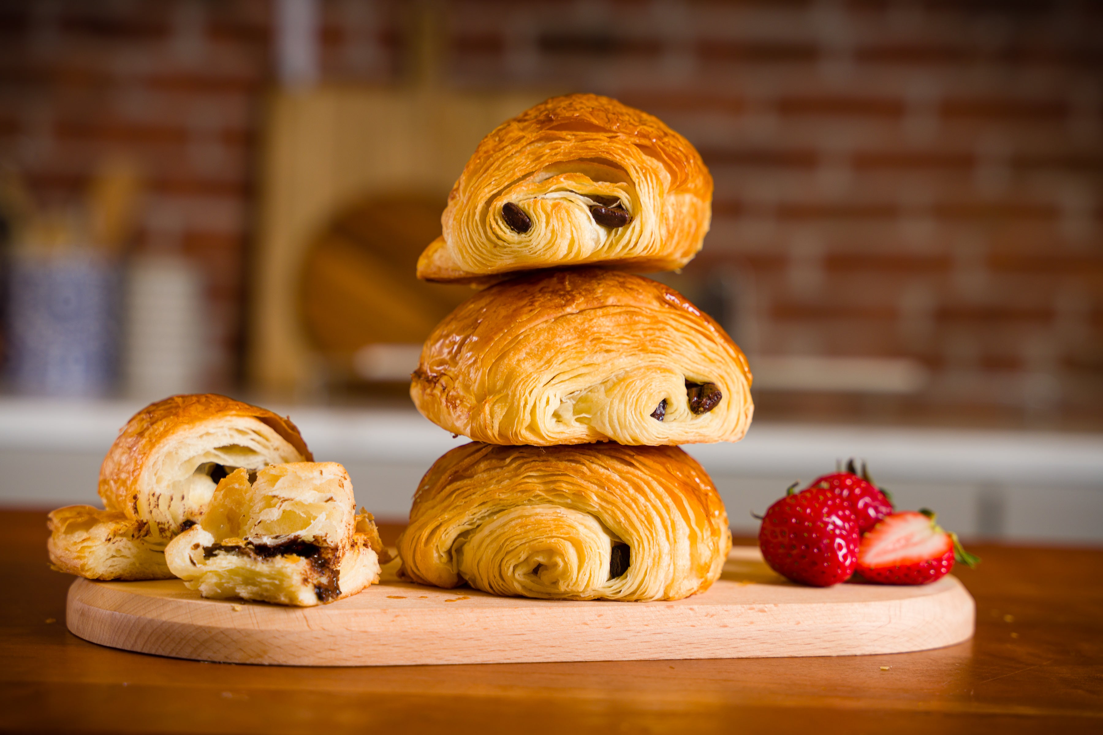 A stack of chocolate croissants on a wooden board with strawberries to the right