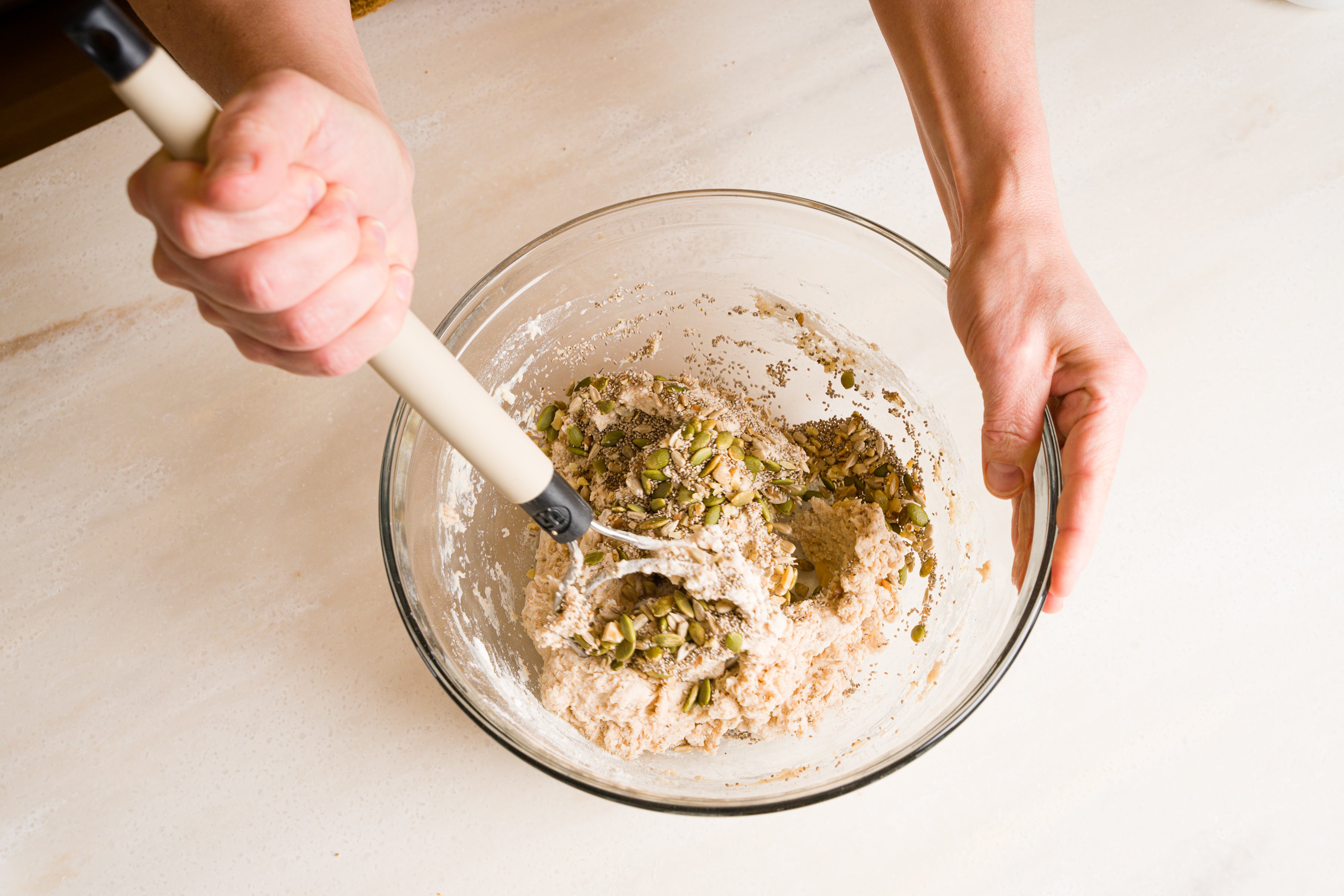 woman's hand stirring buttermilk seed bread dough with dough whisk