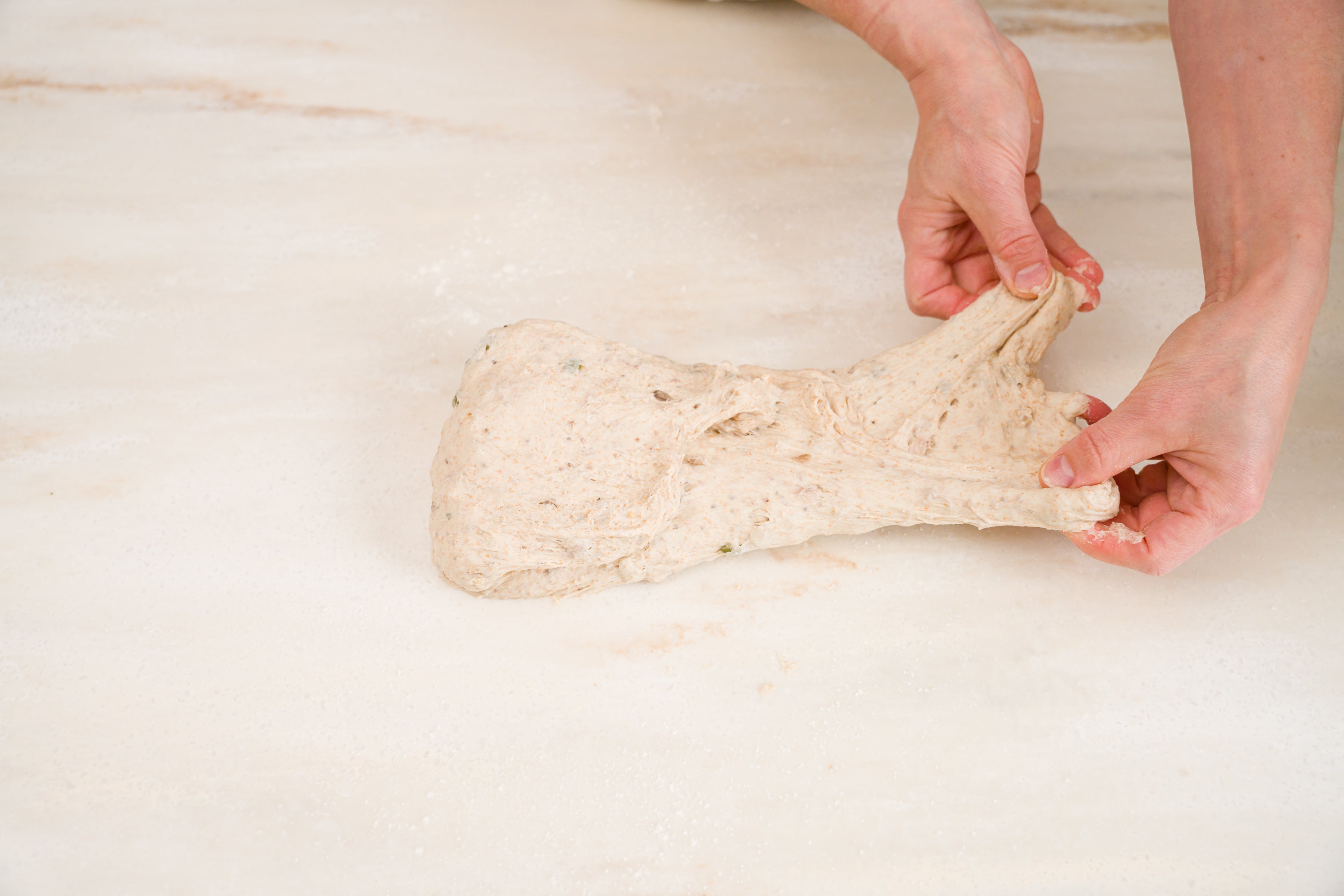 woman's hands folding bread dough on counter