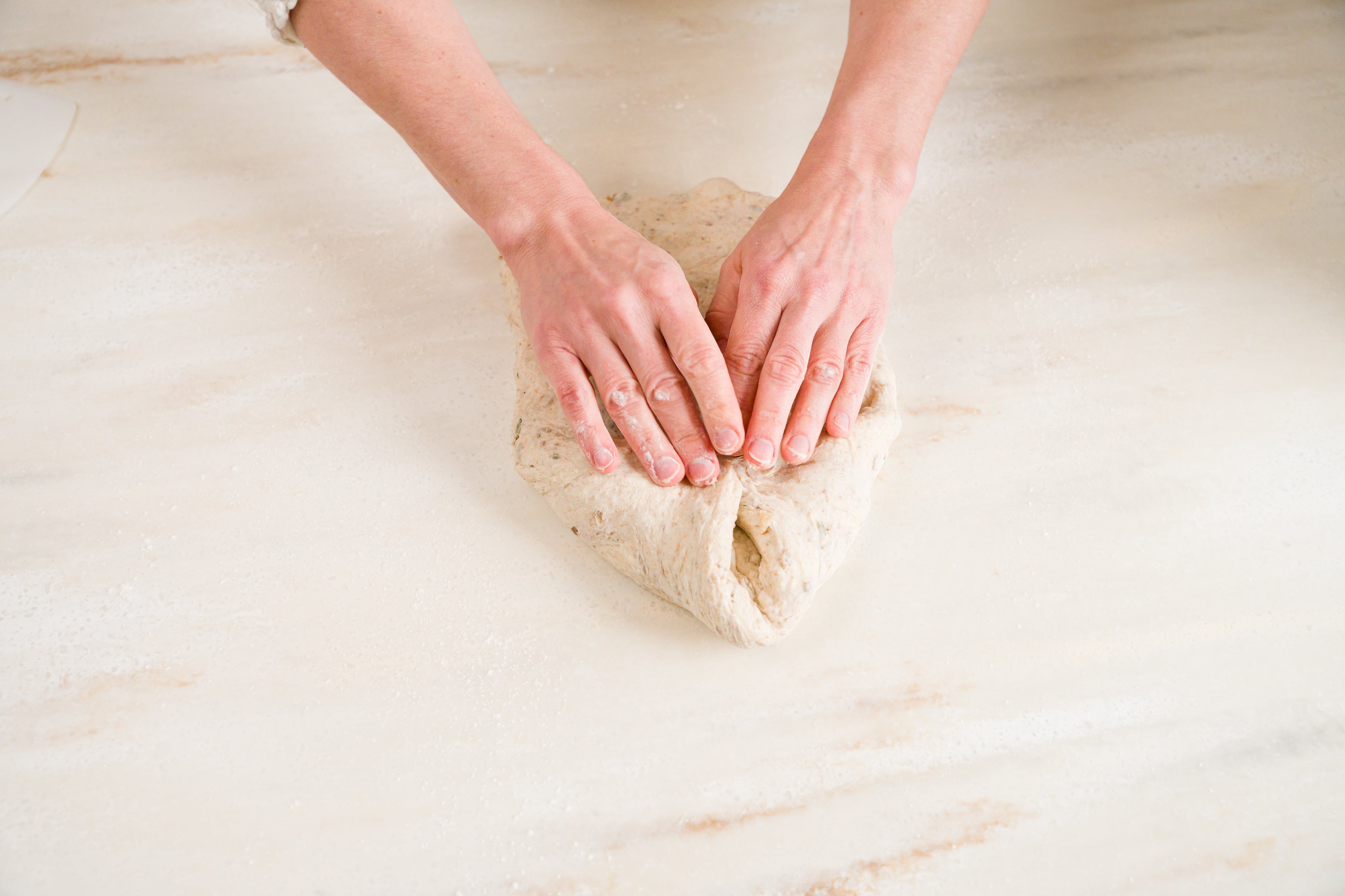 mains de femme pliant les deux coins supérieurs de la pâte à pain vers le centre