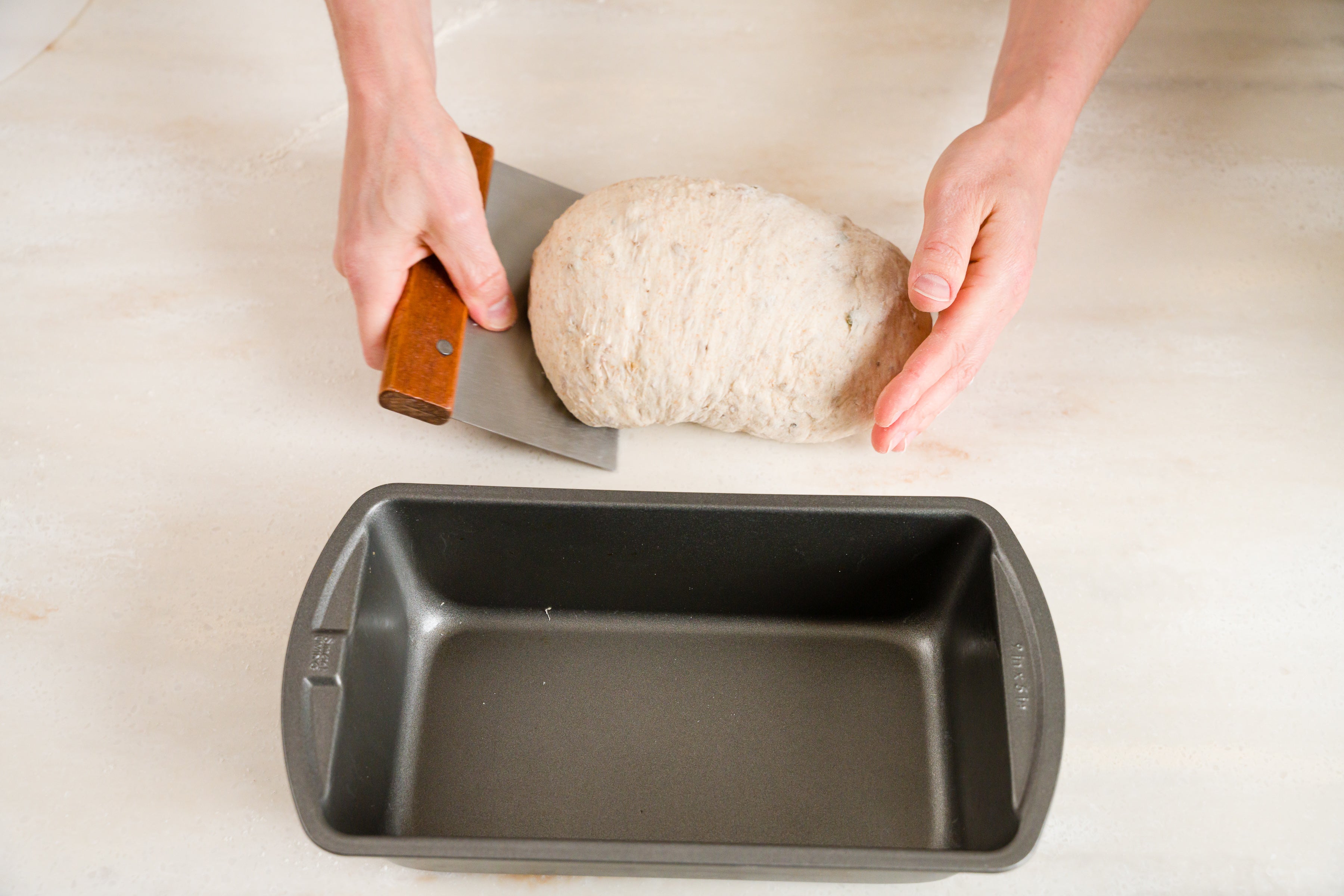 woman's hands lifting shaped loaf into bread pan