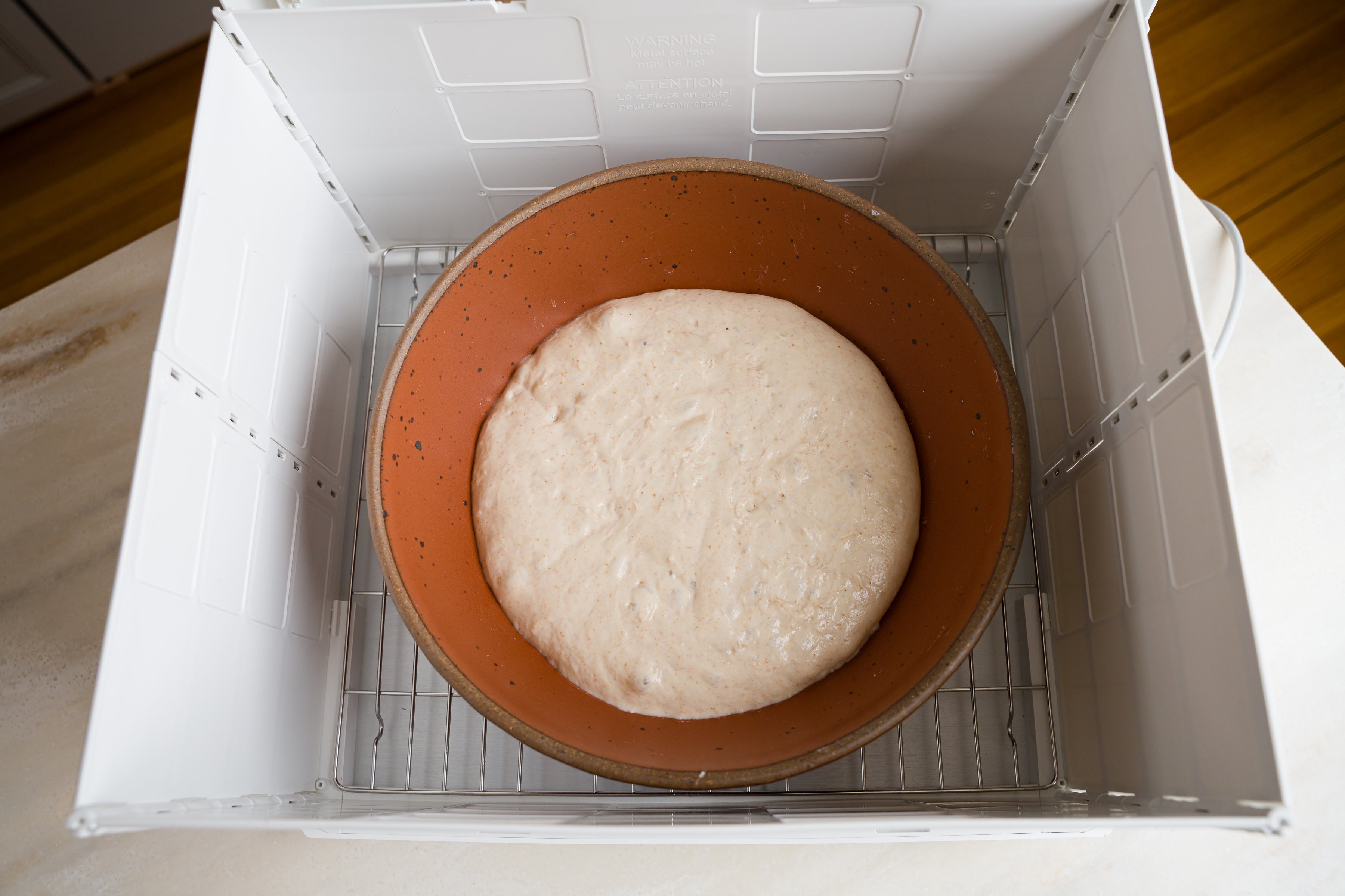 fully risen bread dough inside of brown ceramic bowl inside of folding proofer