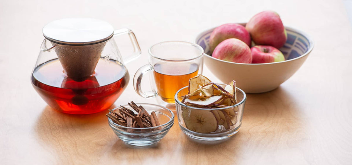 A bowl of apples and apple tea in a glass mug and atea pot