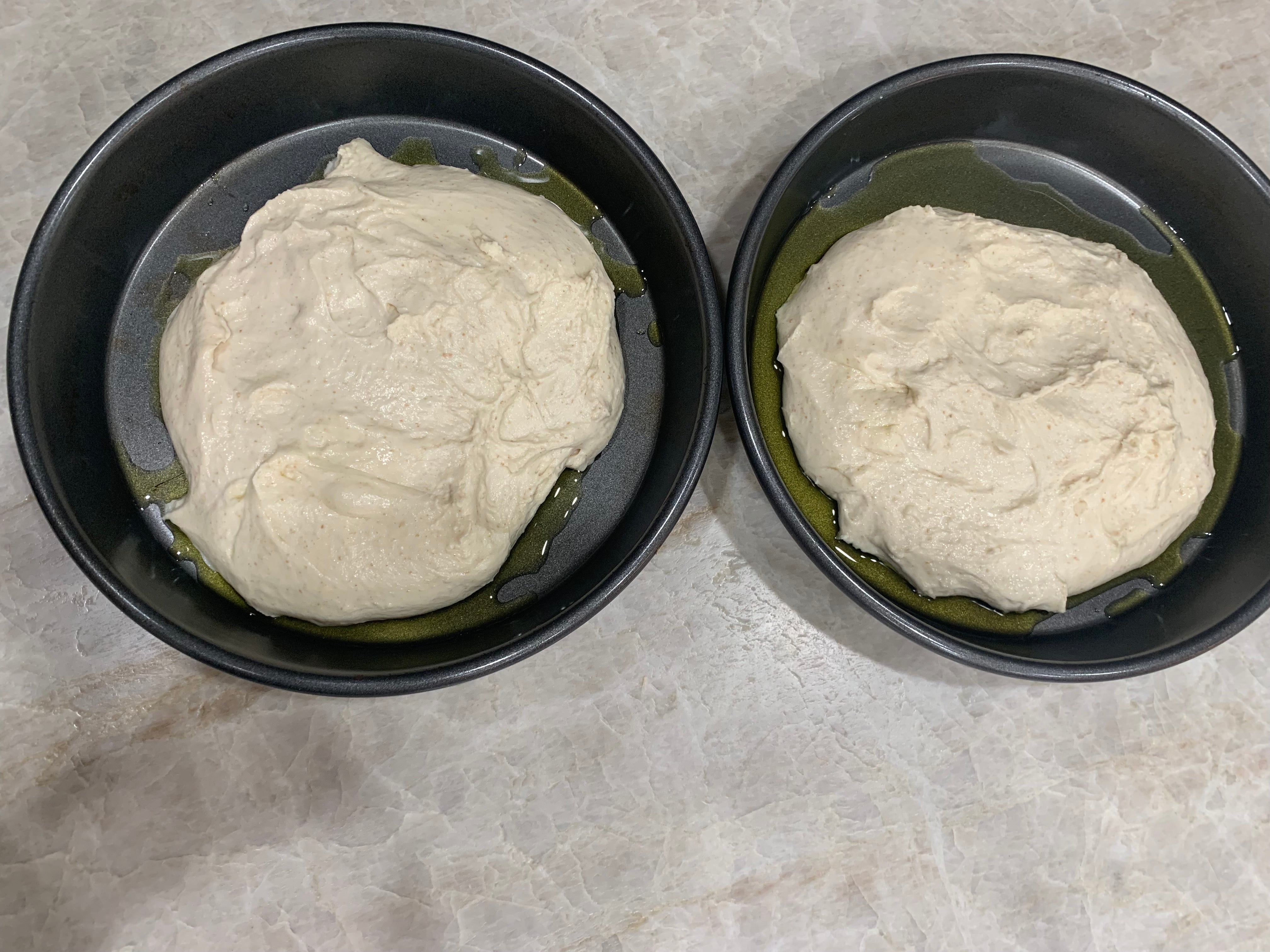 Two oiled pans with dough in them