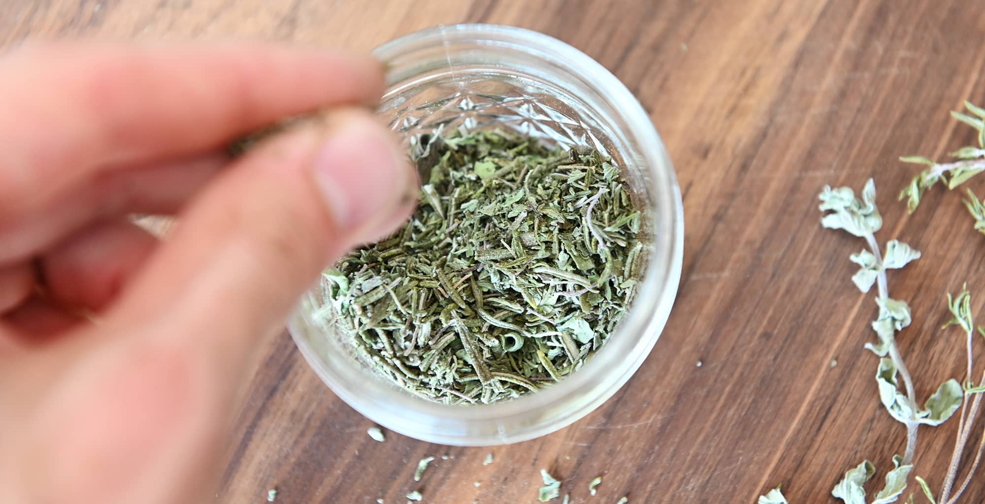 Jar of Italian herb blend next to dehydrated oregano, rosemary, and thyme
