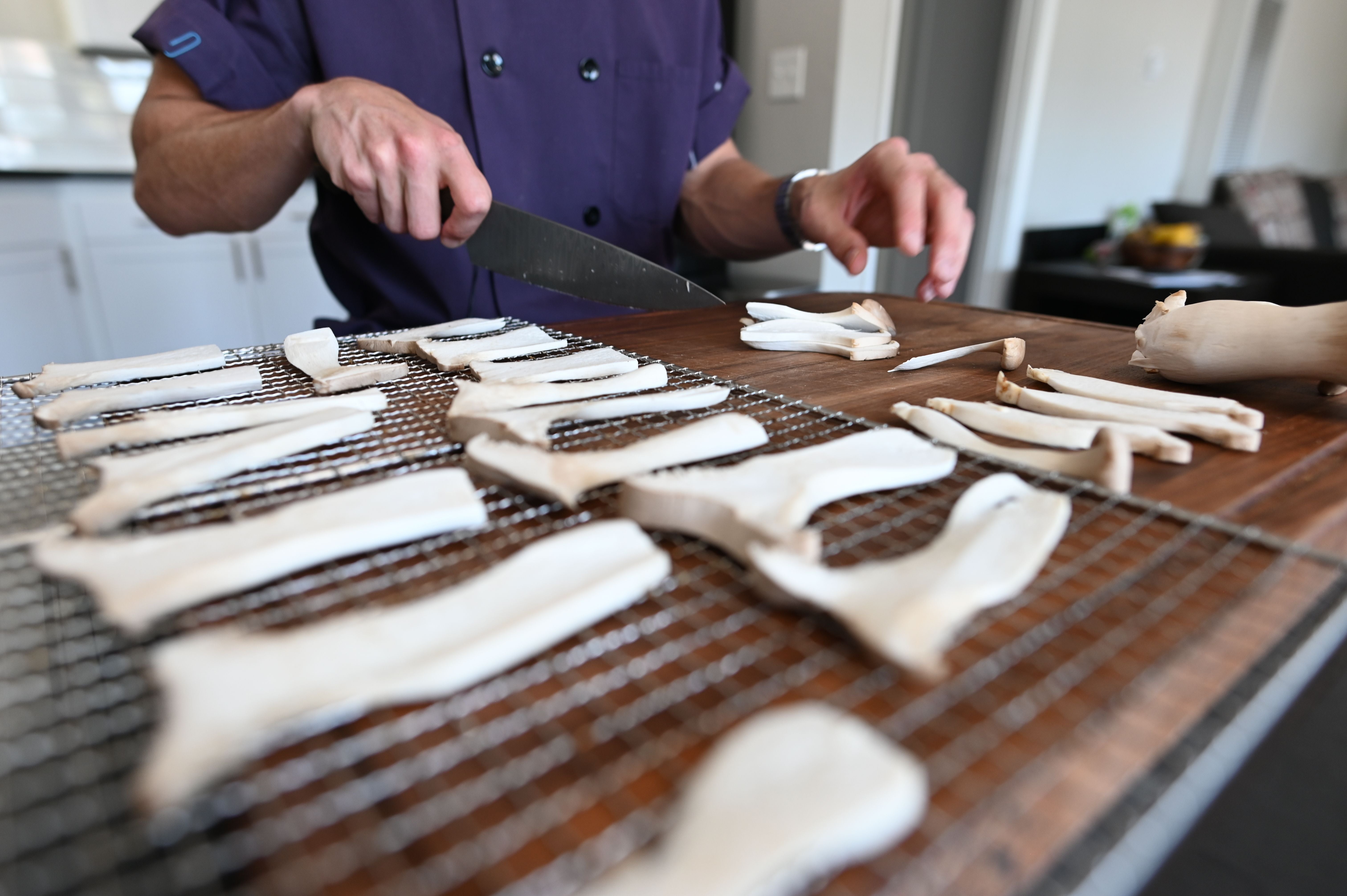 King oyster mushrooms being sliced and placed on dehydrator racks
