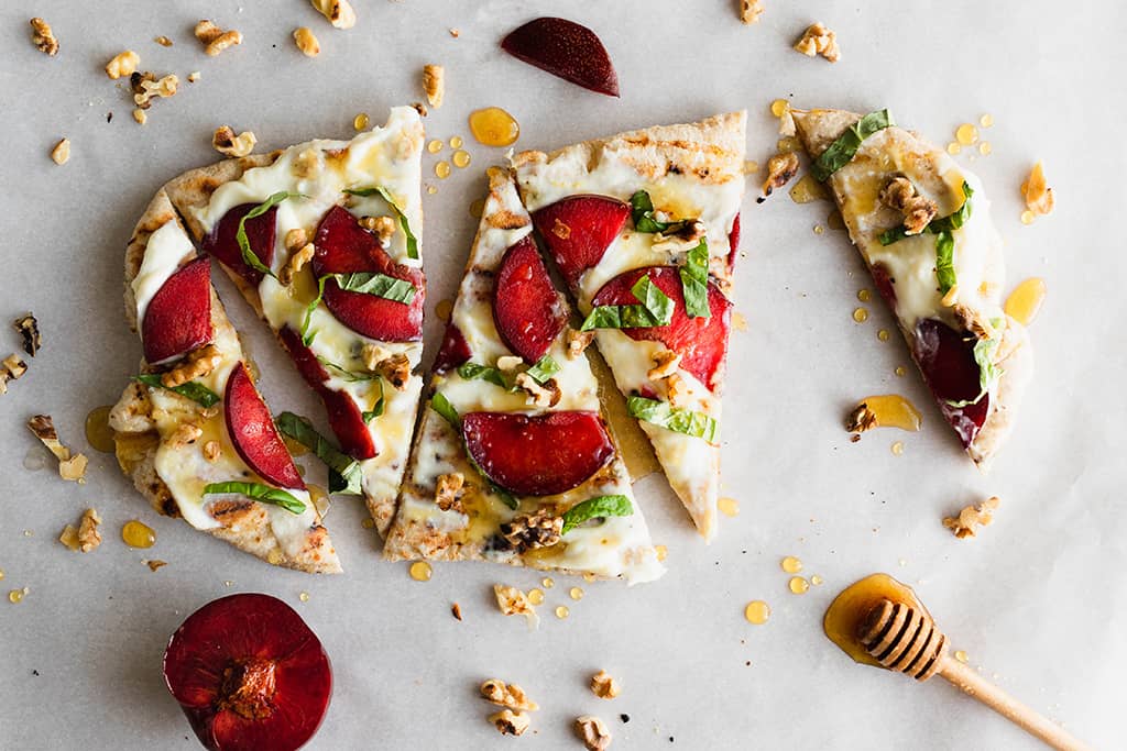 grilled pizza topped with basil, plum, and ricotta cheese