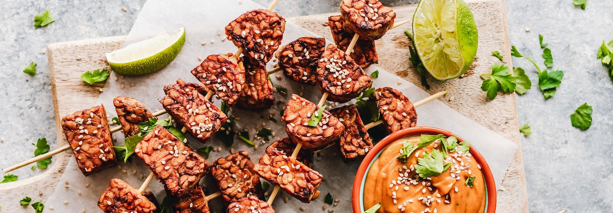 tempeh sliced on skewers with sauce on serving board