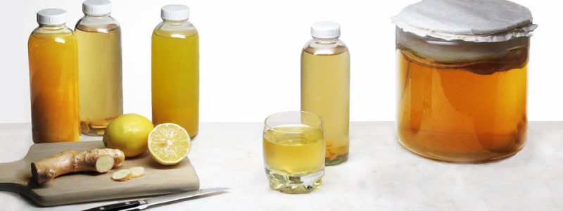 Bottled kombucha with lemon and ginger slices on a cutting board