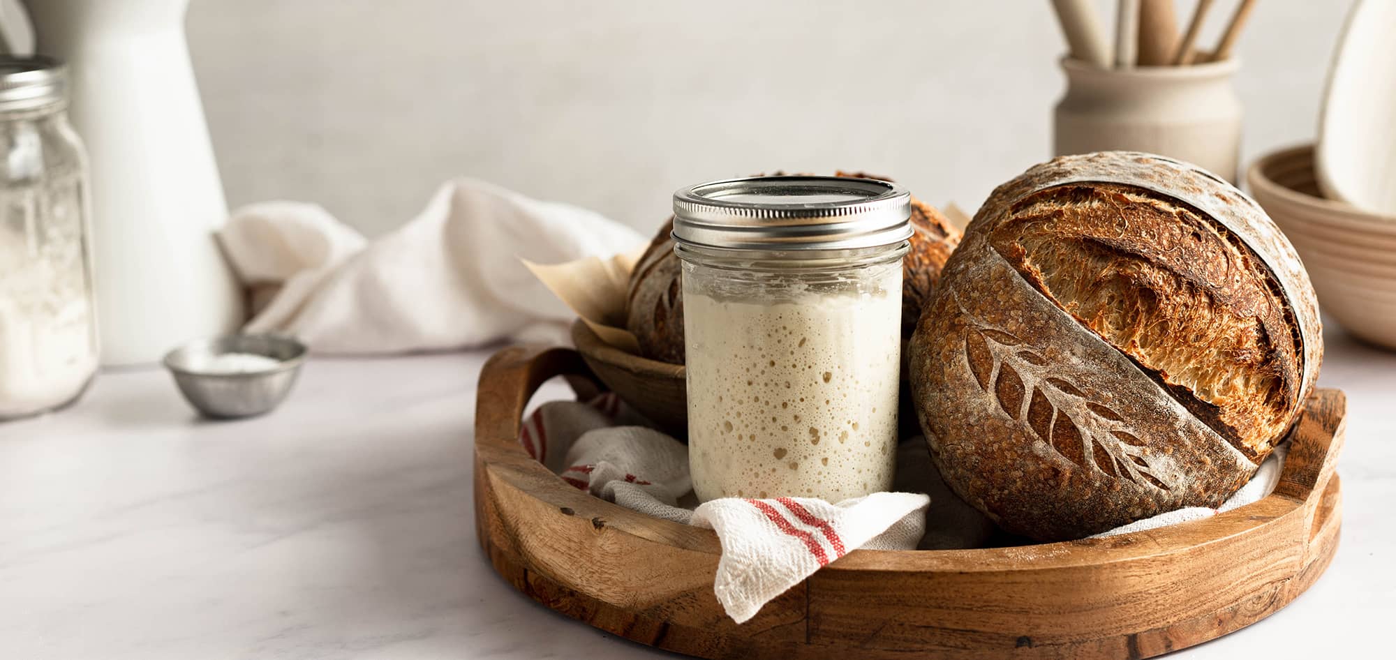 sourdough bread and a jar of sourdough starter on a wooden tray