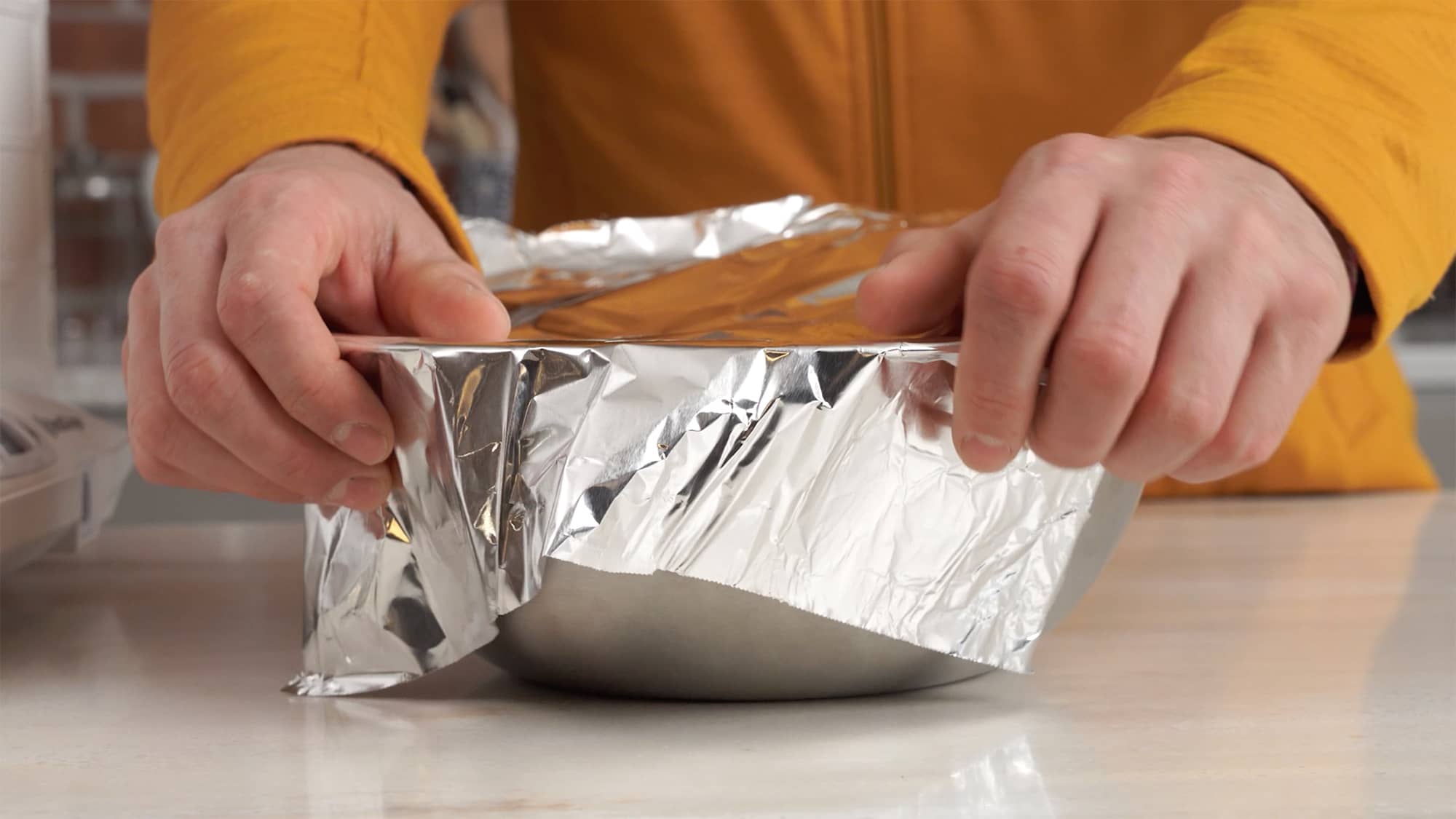 Dough in a stainless steel bowl covered with aluminum foil