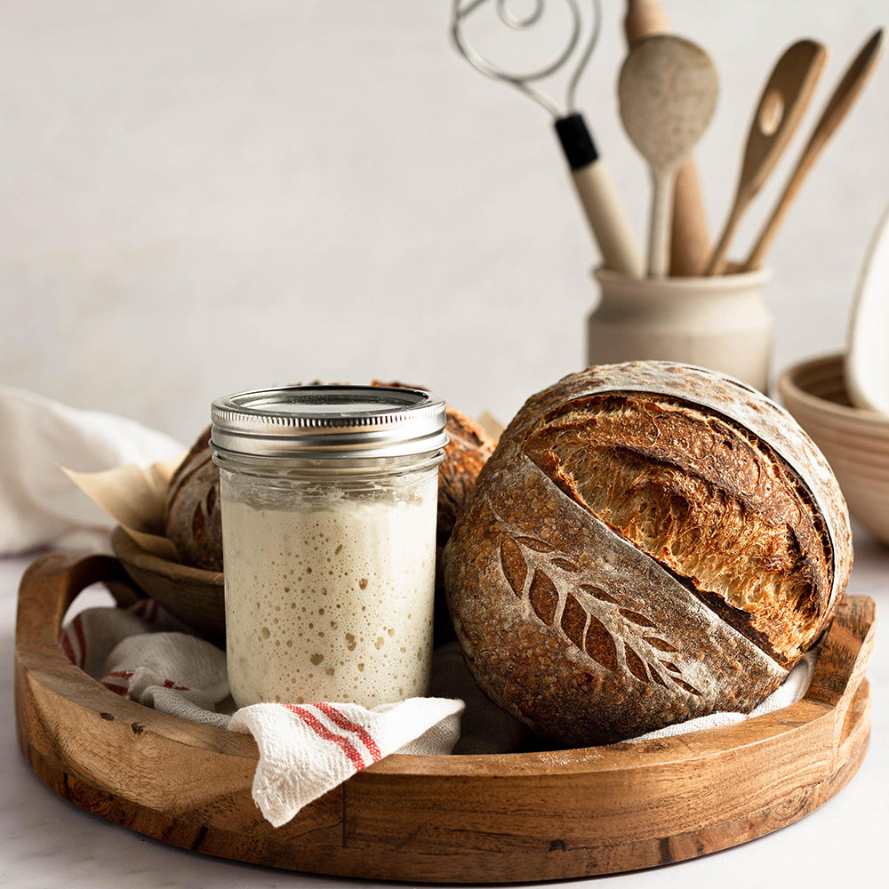 sourdough starter in a jar and sourdough bread in a wooden tray