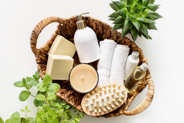 A basket full of bath products like soap, lotion, a scrub brush with greenery accents.